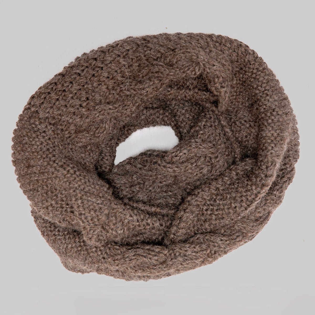 A chunky knit infinity scarf in a warm taupe-brown color, arranged in a loose coil