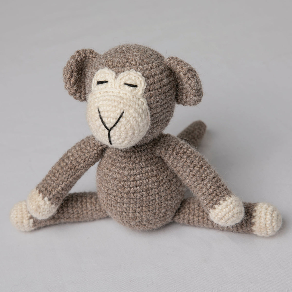 A crocheted stuffed monkey toy sitting cross-legged .