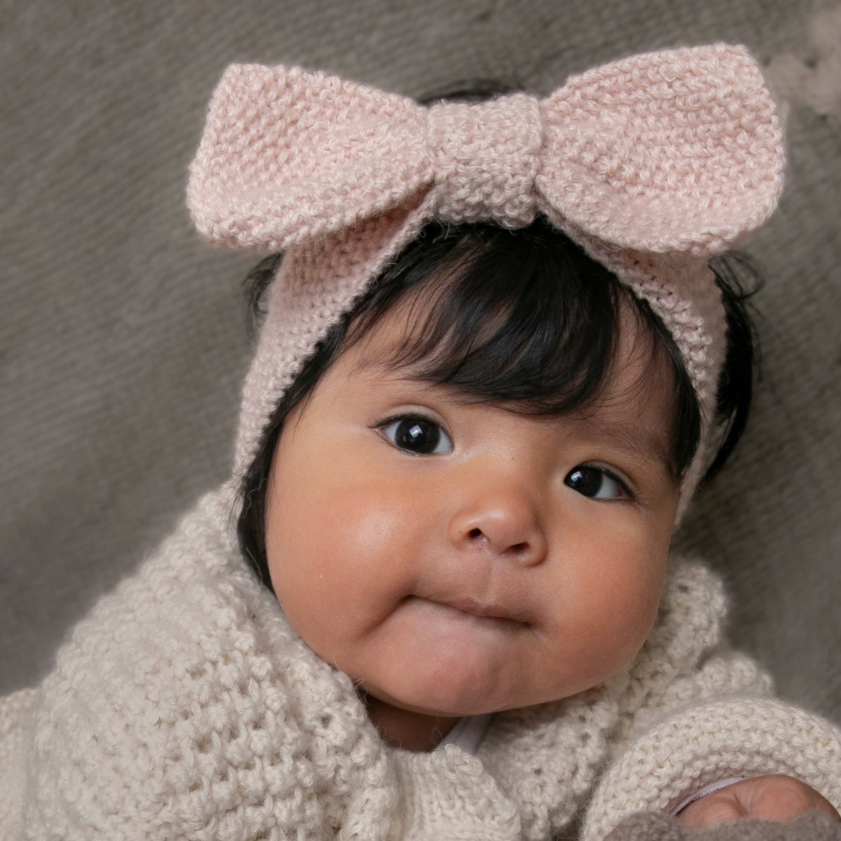 A close-up of a baby wearing a chunky knit matching set consisting of a light pink bow headband