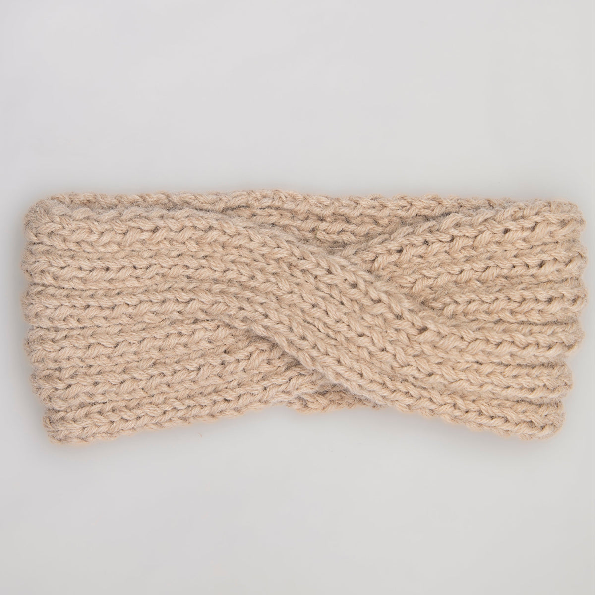 A chunky knit twist-front headband in a light beige color,