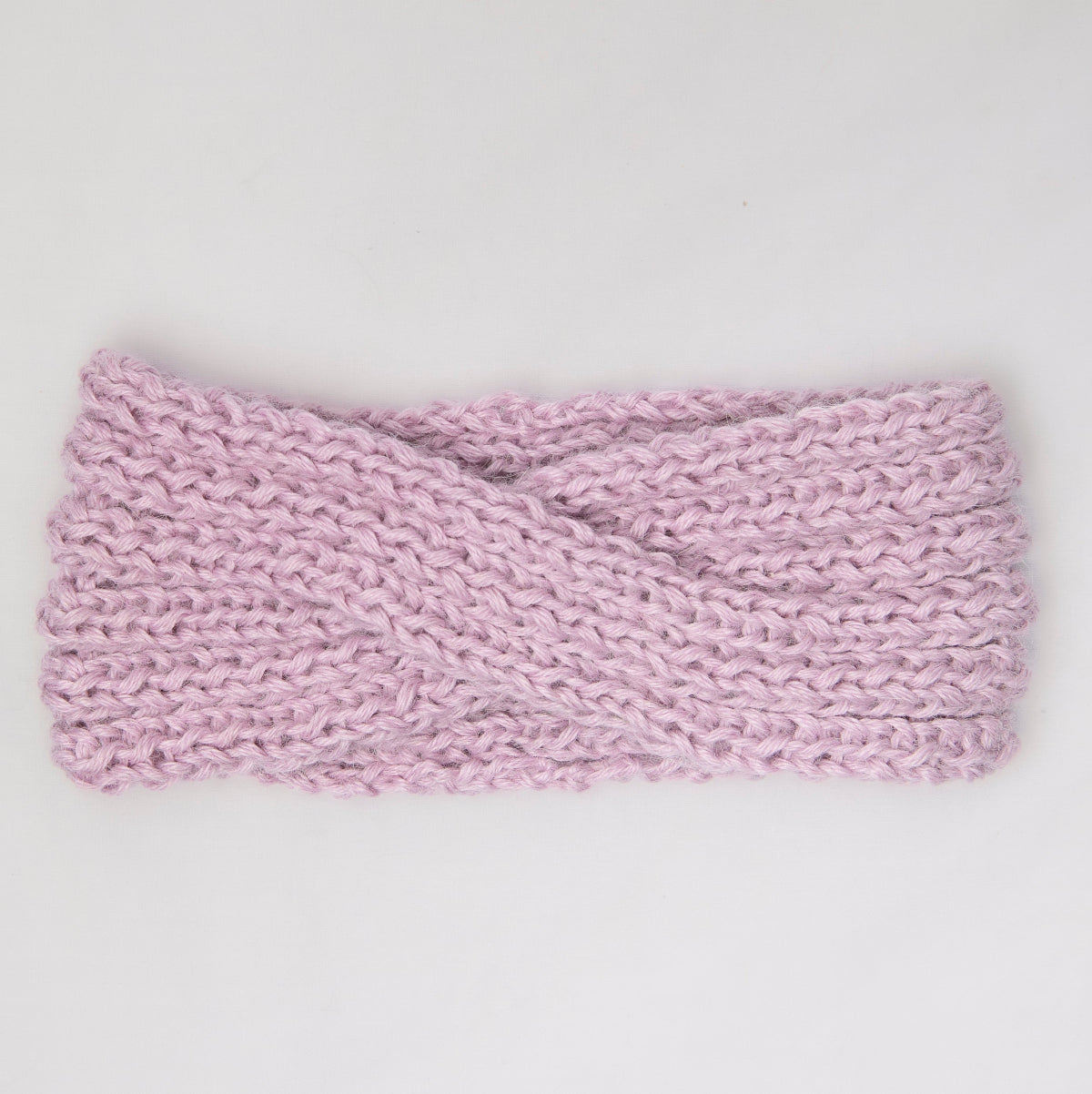 A light pink knitted twist-front headband with a chunky, textured stitch pattern,