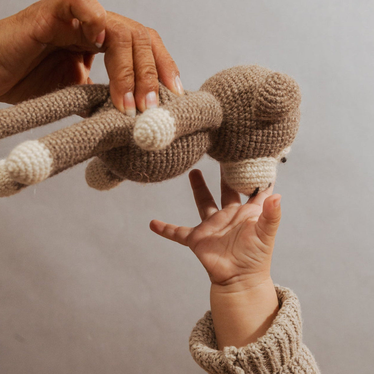 A close-up of a person holding a crocheted stuffed animal with a brown body and cream-colored accents, wearing a beige knit sweater.